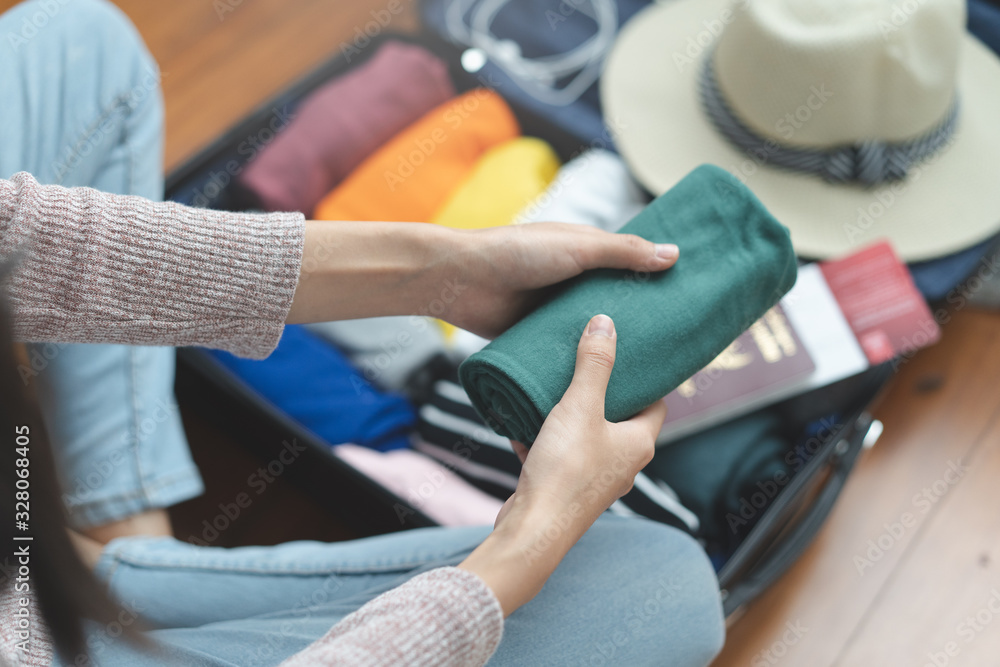 Preparing suitcase for summer vacation trip. Young woman checking accessories and stuff in luggage on the bed at home before travel.
