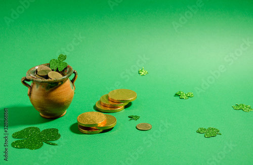 Attributes St. Patrick's Day - a pot of gold stands on a green background, next to it are gold coins and clover leaflets. Horizontal background, soft focus.