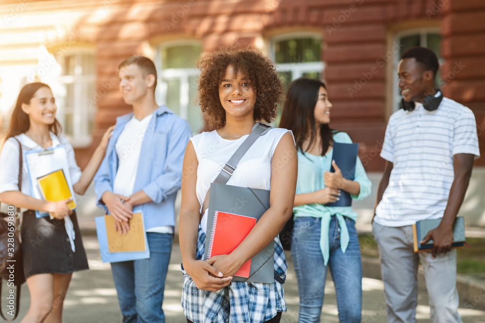 Obraz premium Beautiful african student girl posing outdoors with university friends on background