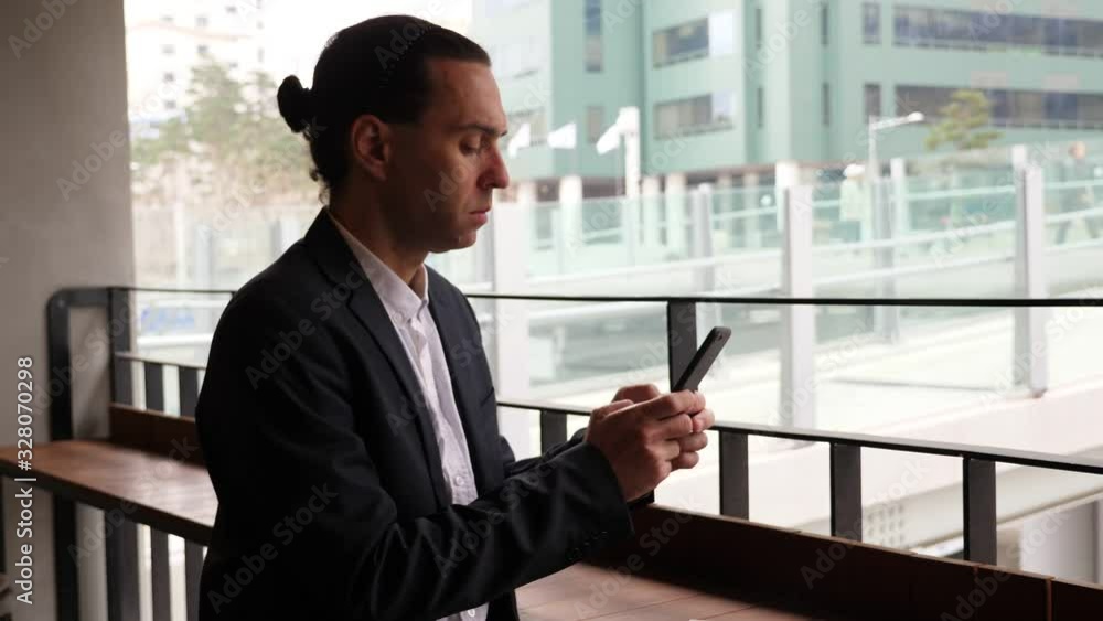 Man focused on smartphone, answer on messages, sitting in cafe against window. Modern urban pedestrian area of central Seoul seen outdoor. Guy wear casual suit and white shirt Man focused on smartphone, answer on messages, sitting in cafe against window. Modern urban pedestrian area of central Seoul seen outdoor. Guy wear casual suit and white shirt