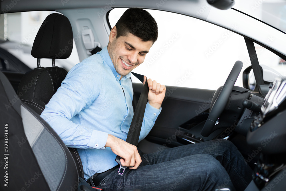 Guy Putting On Seat Belt Sitting In Car In Dealership Guy Putting On Seat Belt Sitting In Car In Dealership