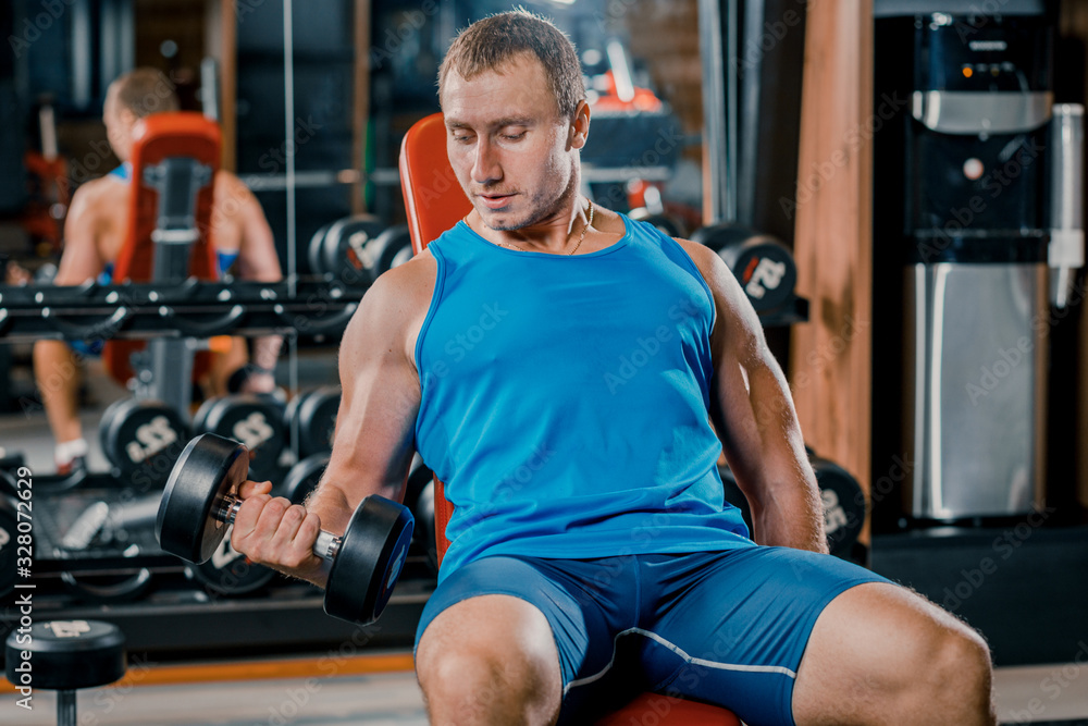 Young muscular guy doing hard exercises with dumbbells on the training bench in the gym Young muscular guy doing hard exercises with dumbbells on the training bench in the gym