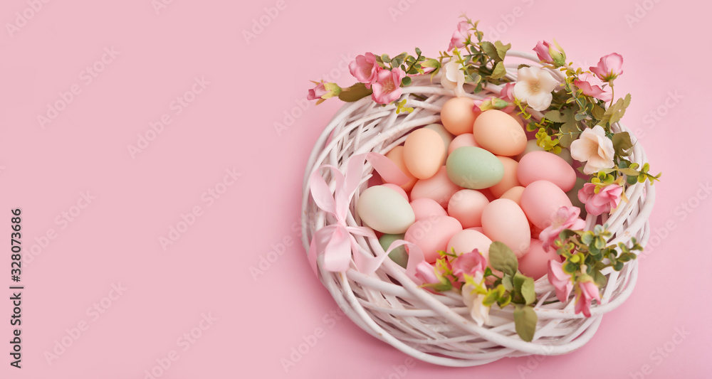 Colorful easter eggs in nest on pastel color background with flowers, copy space. Easter decorations. Easter background with painted eggs in nest, vintage style, top view. Spring greeting card