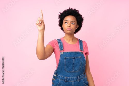 African american woman with overalls over isolated pink background touching on transparent screen