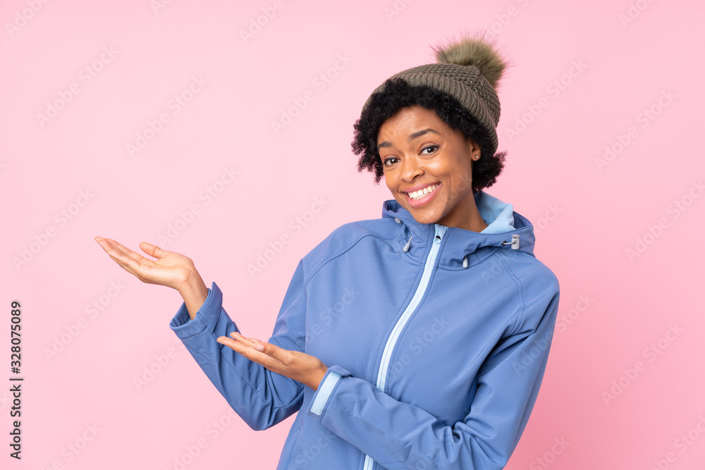 African american woman with winter hat over isolated pink background extending hands to the side for inviting to come African american woman with winter hat over isolated pink background extending hands to the side for inviting to come