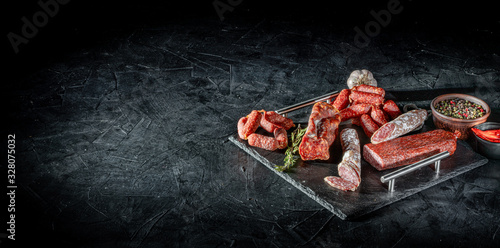Different kinds of delicious smoked dried sausages, salami or kabanos on dark background photo