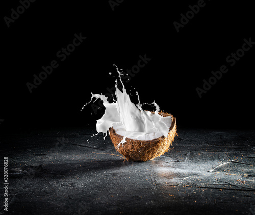 Cracked coconut with splashes of milk on dark background