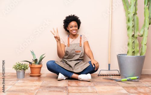 Gardener woman sitting on the floor happy and counting three with fingers