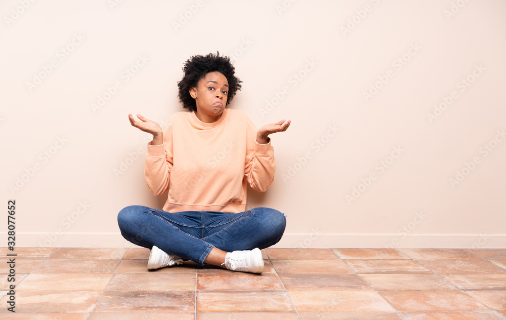 African american woman sitting on the floor having doubts while raising hands African american woman sitting on the floor having doubts while raising hands