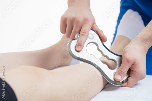 The doctor makes a massage with the Blade tool. Increased mobility of the soft tissues of the leg. White background, isolate