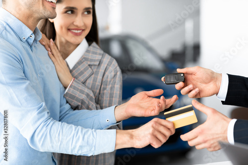 Couple Buying Car Giving Seller Credit Card In Dealership Office