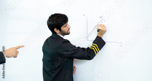 Young pilot man in uniform writing graph by marker on whiteboard having discussion with business man about aviation businessn,startup,business team,people,economics,analytics and statistics concept, photo
