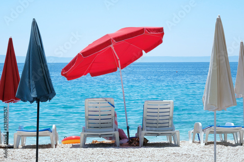Red beach umbrella and chaise for relax and comfort on sea coast. Happy summer vacations and  tourism concept. Paid service on waterscape beaches.