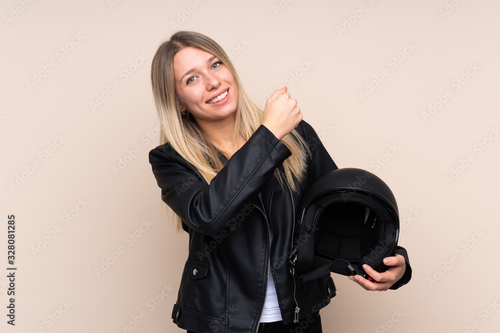 Young blonde woman with a motorcycle helmet over isolated background celebrating a victory Young blonde woman with a motorcycle helmet over isolated background celebrating a victory