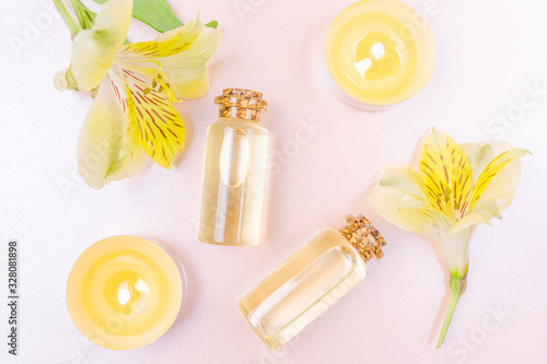 The concept of aromatherapy  spa. Bottles with floral essential oil  a yellow flower and candles on a pastel pink background. Cozy flat lay in bright colors. Copyspace  minimalism  top view.