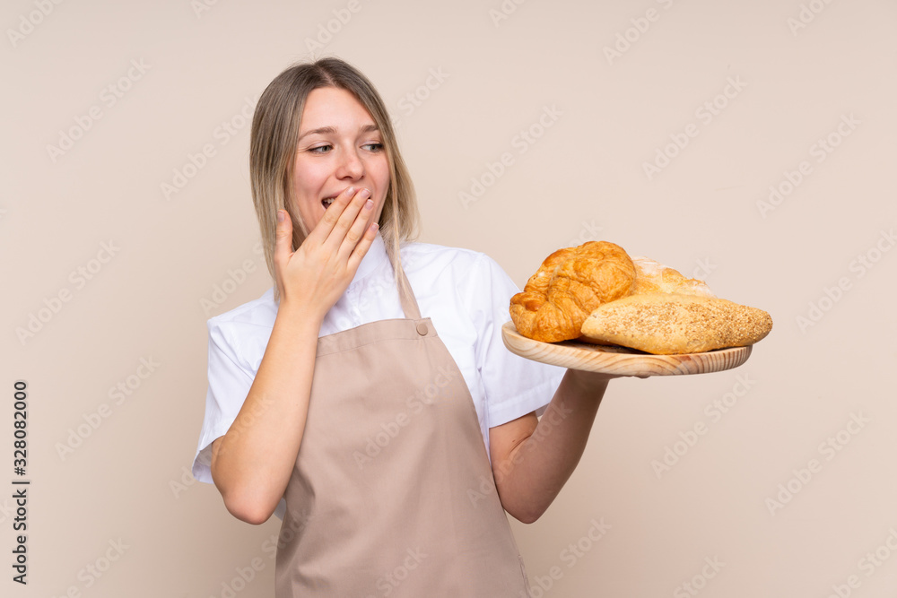 Young blonde girl with apron. Female baker holding a table with several breads with surprise and shocked facial expression Young blonde girl with apron. Female baker holding a table with several breads with surprise and shocked facial expression