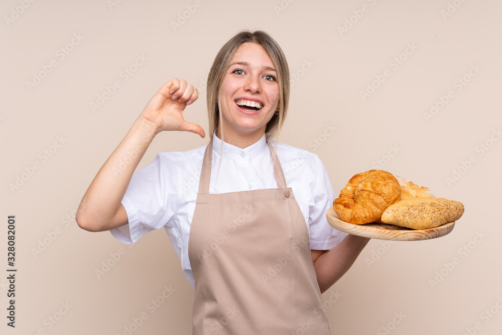 Young blonde girl with apron. Female baker holding a table with several breads proud and self-satisfied Young blonde girl with apron. Female baker holding a table with several breads proud and self-satisfied