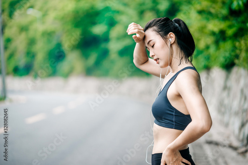 Sporty young Asian woman get tired after running on sidewalk in morning. Health conscious concept with copy space.