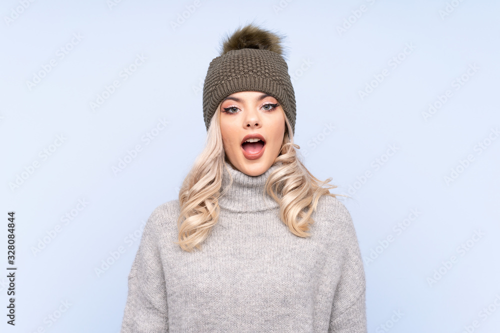 Young teenager girl with winter hat over isolated blue background with surprise facial expression Young teenager girl with winter hat over isolated blue background with surprise facial expression