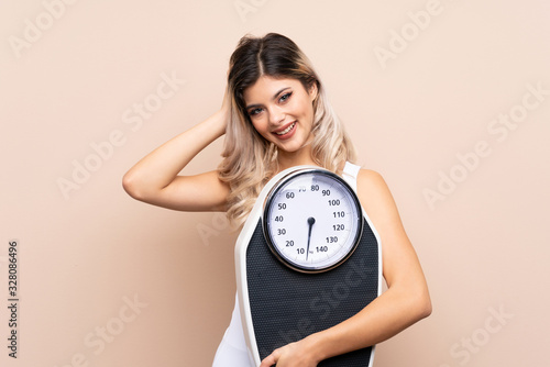 Teenager girl with weighing machine over isolated background holding a weighing machine and pointing to the front