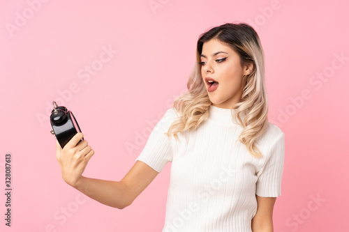 Teenager girl over isolated pink background holding vintage alarm clock