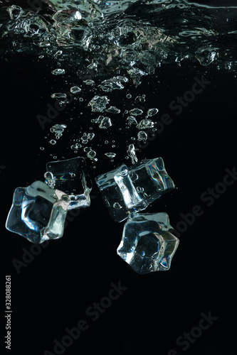 Ice cubes are thrown into the water. Frosty freshness. Ice on a black background. Artificial acrylic ice. Cocktail with ice