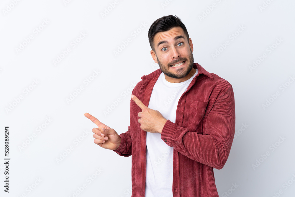 Young handsome man with beard wearing a corduroy jacket over isolated white background frightened and pointing to the side Young handsome man with beard wearing a corduroy jacket over isolated white background frightened and pointing to the side