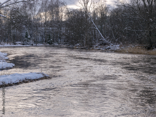 winter landscape with wild fast flowing river, snow covered land