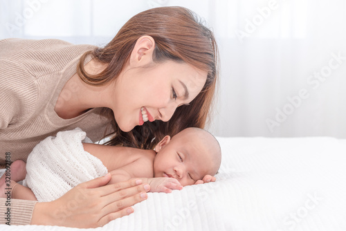 Close up beautiful young asian mother looking her newborn one month baby sleep in bed. Healthcare and medical love asia woman lifestyle mother's day concept.