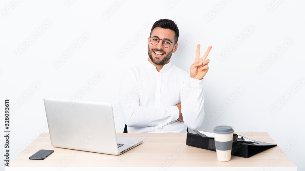 Young businessman in a workplace smiling and showing victory sign Young businessman in a workplace smiling and showing victory sign