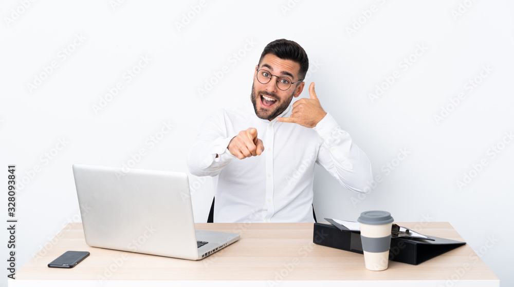 Young businessman in a workplace making phone gesture and pointing front Young businessman in a workplace making phone gesture and pointing front