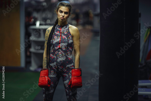 Tattooed young Jewish woman Thai boxer in sports clothing. Muscular fitness model with braids looking at camera photo