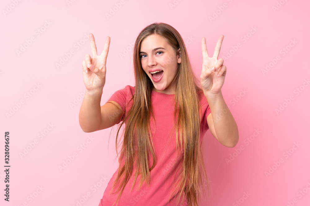 Teenager blonde girl over isolated pink background smiling and showing victory sign Teenager blonde girl over isolated pink background smiling and showing victory sign