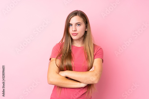Teenager blonde girl over isolated pink background keeping arms crossed