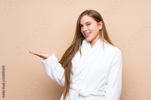 Teenager girl in a bathrobe over isolated background holding copyspace imaginary on the palm