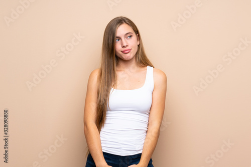 Teenager blonde girl over isolated background making doubts gesture looking side