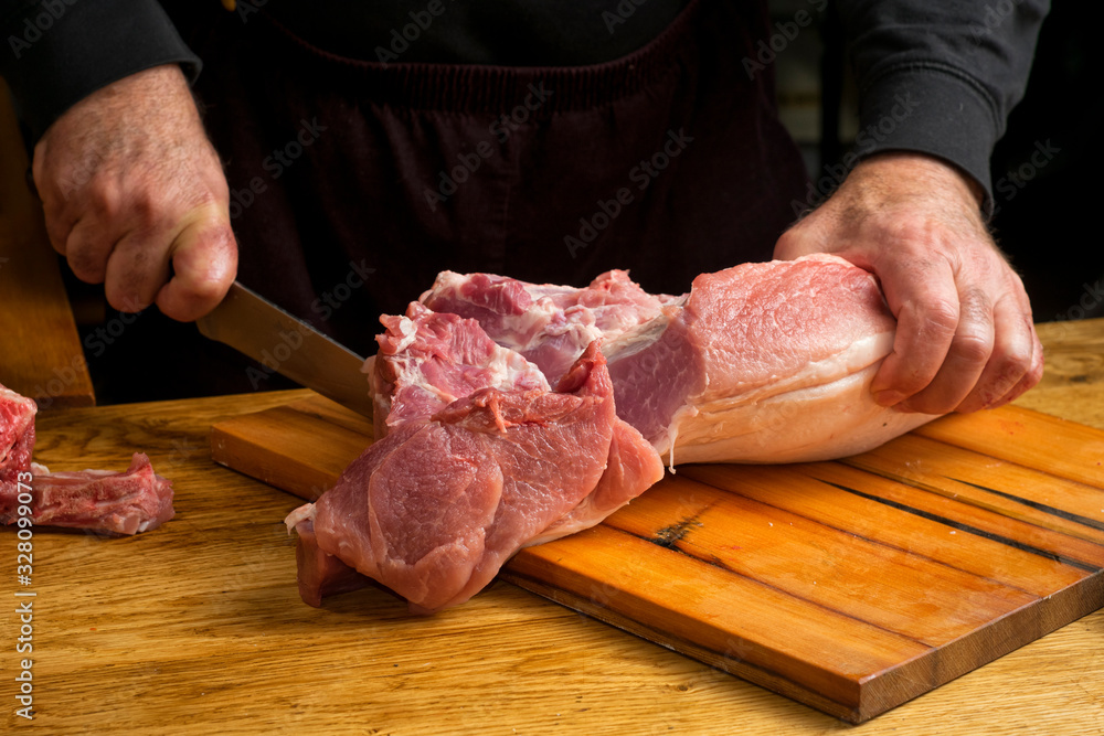 A male chef cuts a piece of pork carcass on a cutting board with a large knife.