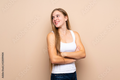 Teenager blonde girl over isolated background with arms crossed and happy