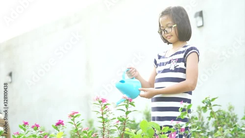 Little Asian girl watering the flower plant by watering can in the sunny day.