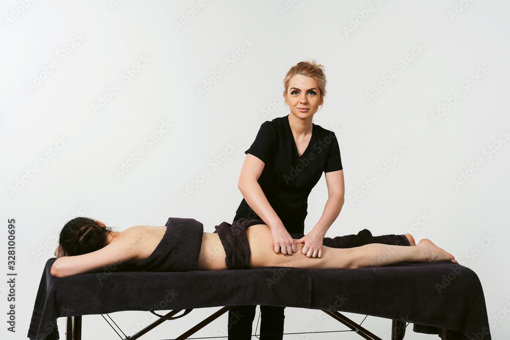 Funny fat burning massage. Portrait of cheerful woman masseur in uniforme near massage table with woman patient in wellness center. White background isolated Funny fat burning massage. Portrait of cheerful woman masseur in uniforme near massage table with woman patient in wellness center. White background isolated