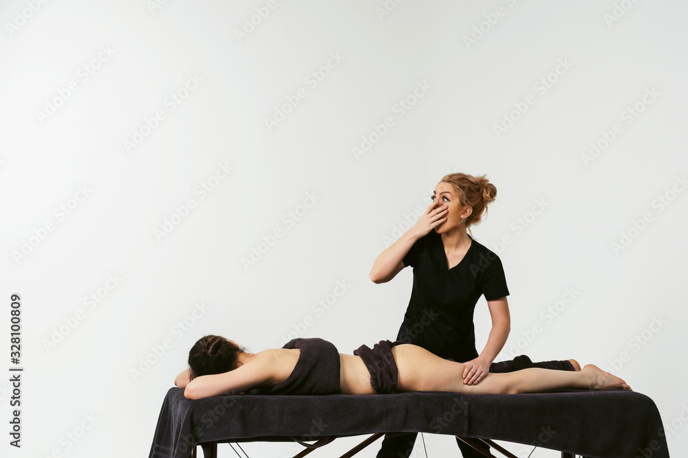 Funny fat burning massage. Portrait of cheerful woman masseur in uniforme near massage table with woman patient in wellness center. White background isolated Funny fat burning massage. Portrait of cheerful woman masseur in uniforme near massage table with woman patient in wellness center. White background isolated