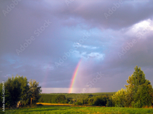 Rainbow in dark cloudy sky above meadow and forest an picturesque natural landscape background