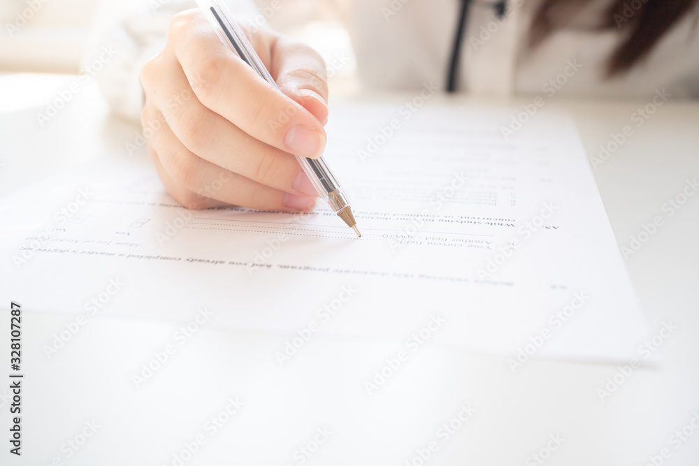 Female hands hold a pen, write on a sheet of paper, fill out a form on a table Female hands hold a pen, write on a sheet of paper, fill out a form on a table