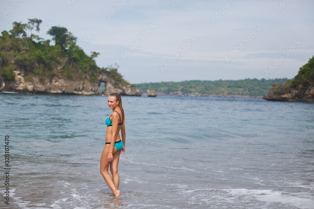 girl in a blue swimsuit walks on a tropical beach