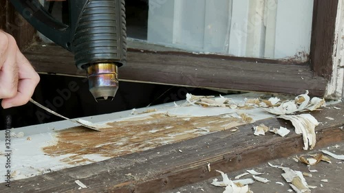 Vintage window restoration, worker using putty knife and electric heat gun to remove old paint