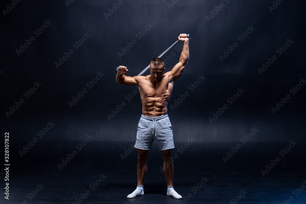 Muscular man doing calisthenic exercise with power band isolated on the black background