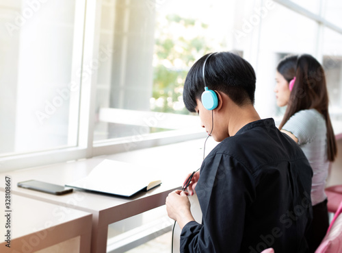 In selecive focus of young teenager wearing blue headphone on her head,reading book,beside window,blurry lignt around photo