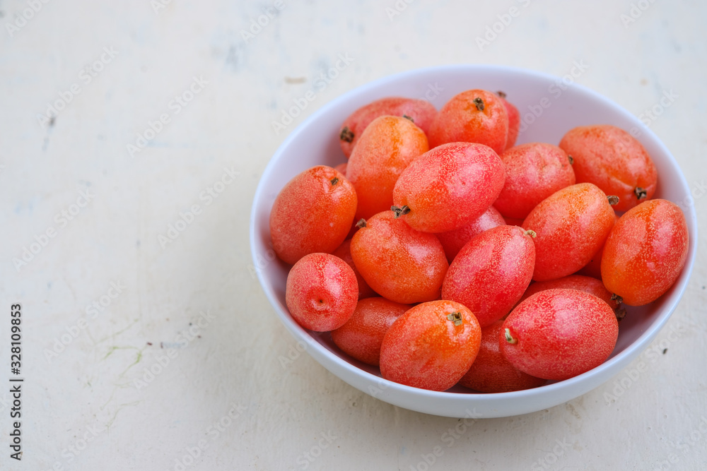 Elaeagnus berry in white bowl on backdrop,copy space,fruit of thailand Elaeagnus berry in white bowl on backdrop,copy space,fruit of thailand