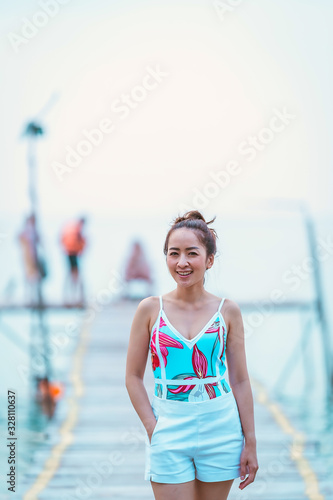 Asian beautiful girl in swimming dress standing posing a relaxing on the wood bridge with blur sea in evening time © etemwanich