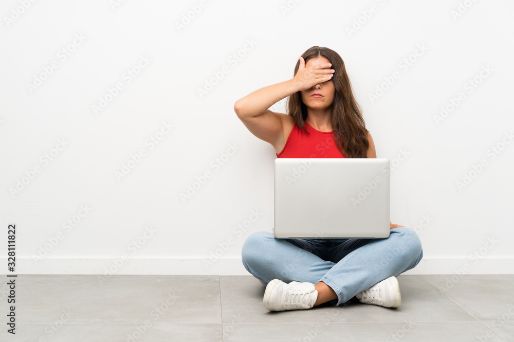 Young woman with a laptop sitting on the floor covering eyes by hands Young woman with a laptop sitting on the floor covering eyes by hands